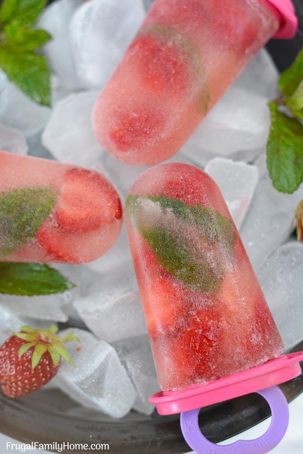 Homemade popsicles in a bowl of ice with mint and strawberries.
