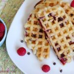 Cooked homemade waffles ready to eat with a side of raspberries.